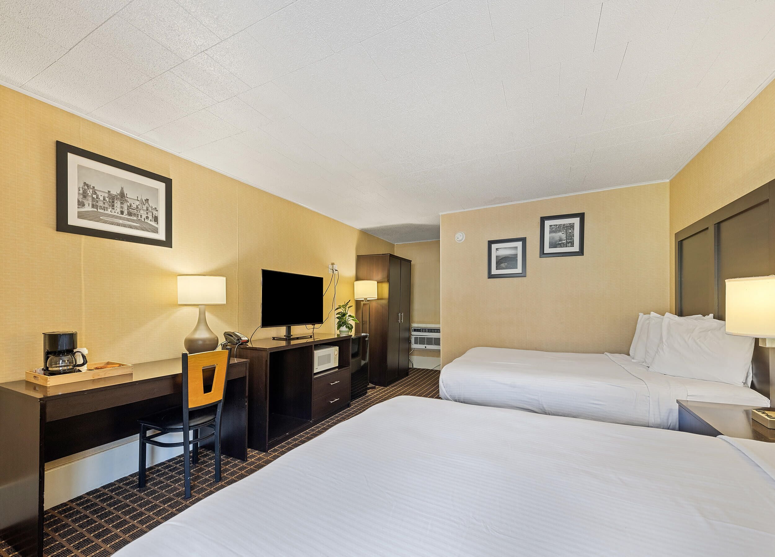 A hotel room with a bed, desk, chair, television, and two framed pictures on the wall.