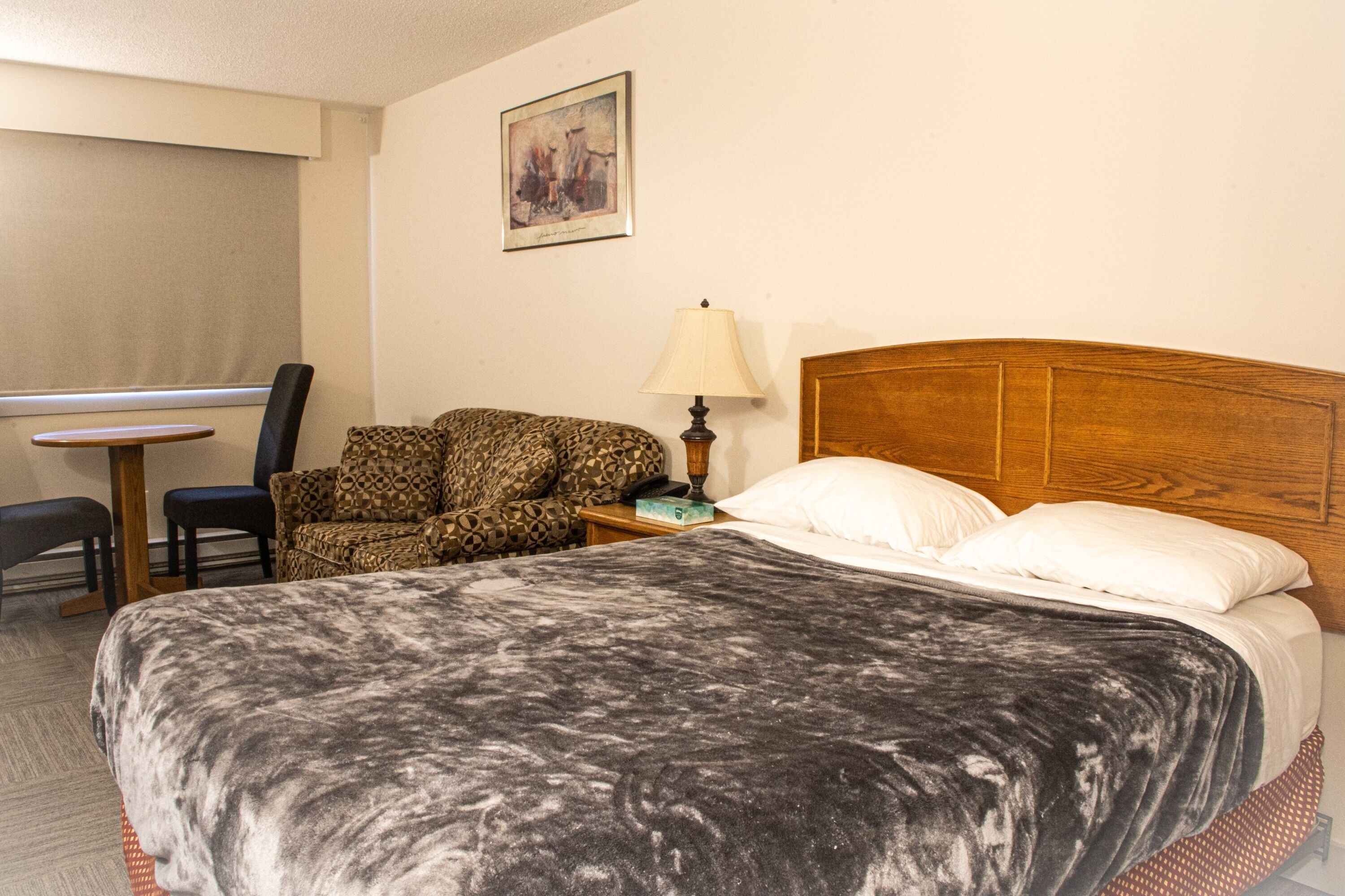 A hotel room with a bed, a chair, a small table, and a lamp.