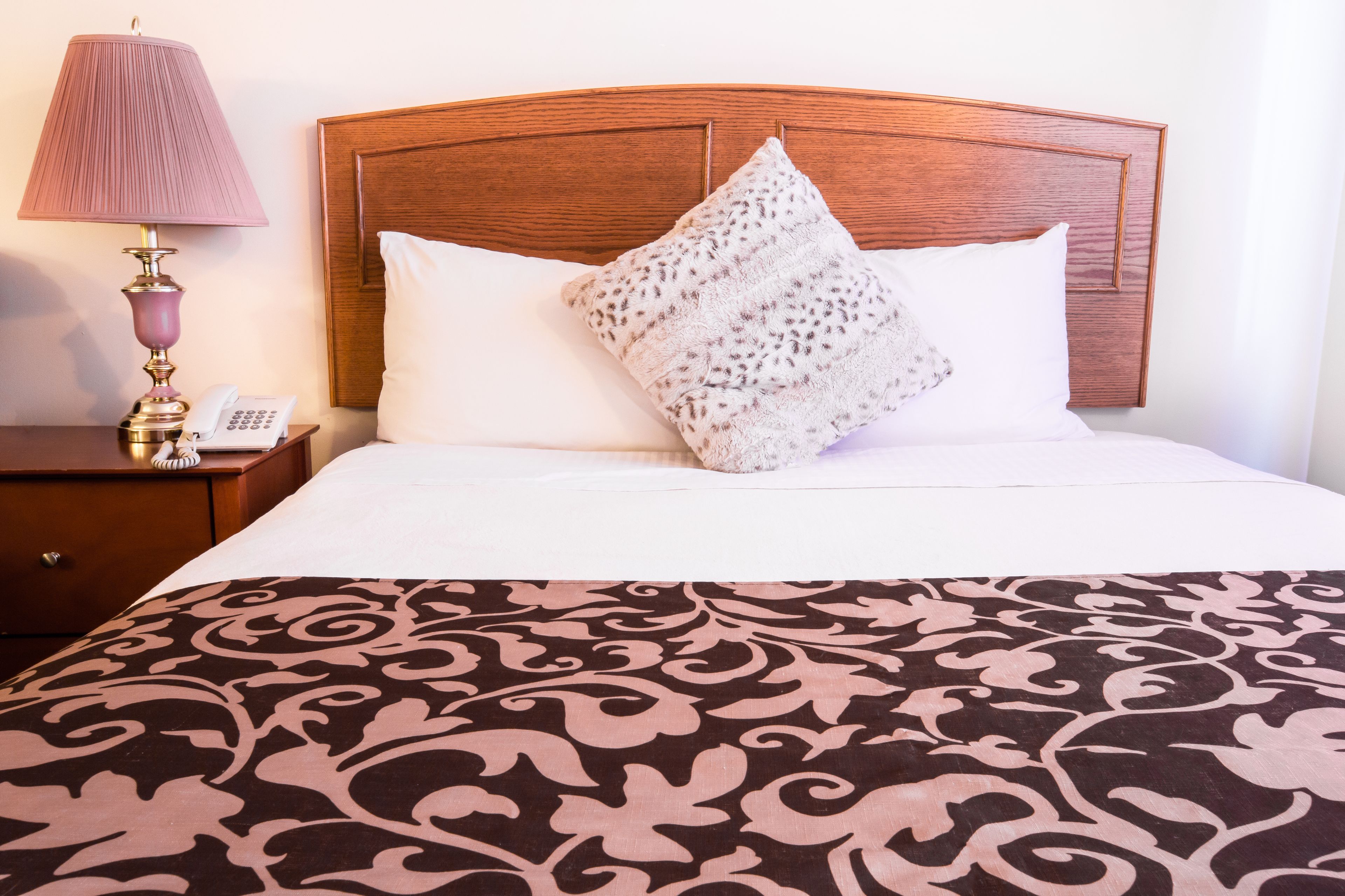 Een netjes opgemaakt bed met een bedsprei met patroon, een houten hoofdbord en een bedlampje.