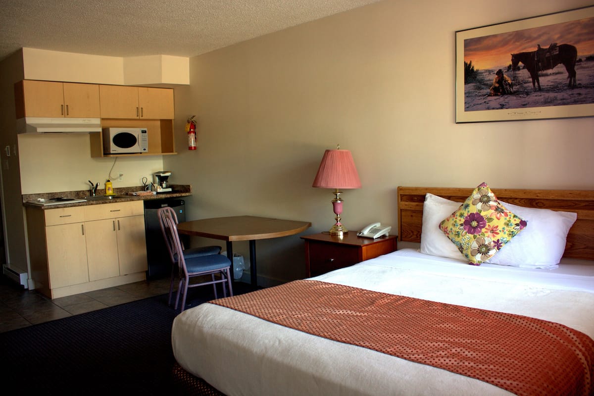 A hotel room with a bed, a desk, a chair, a microwave, a lamp, and a painting on the wall.