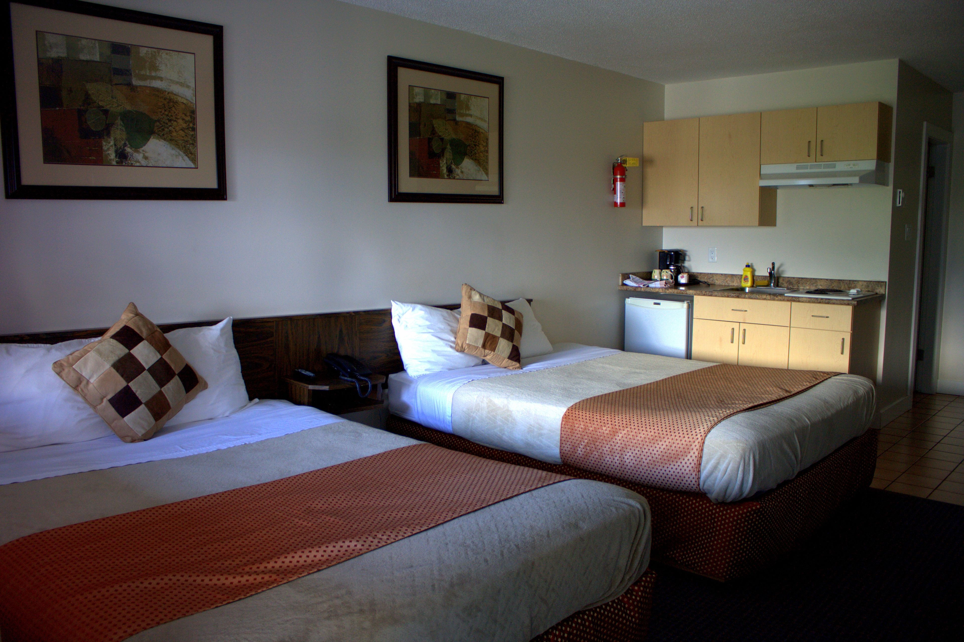 A hotel room with two beds, a kitchenette, and artwork on the walls.