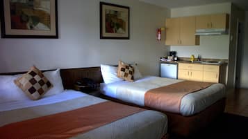A hotel room with two beds, a kitchenette, and artwork on the walls.