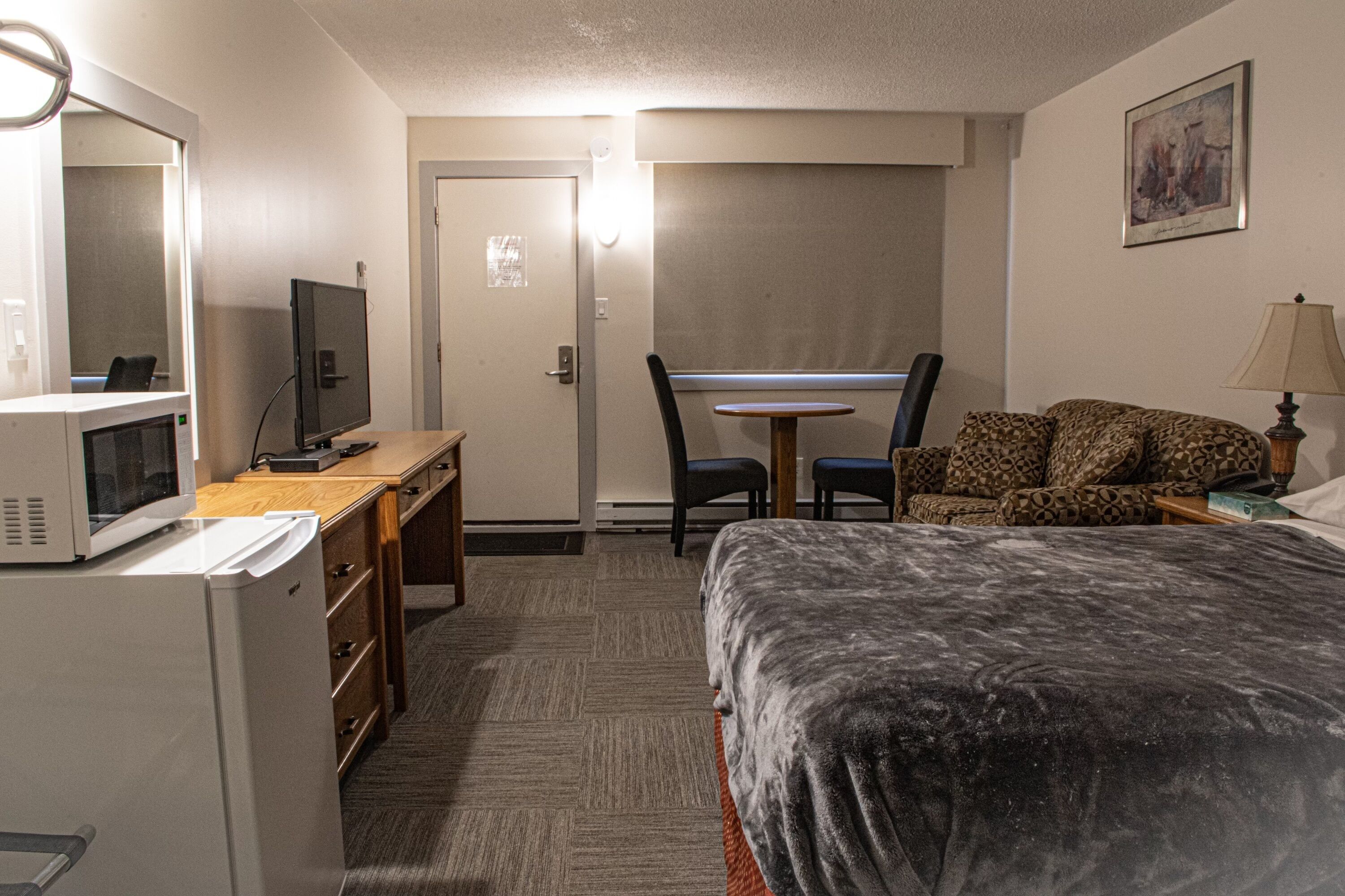 Una habitación de hotel con cama, escritorio con computadora, microondas, sillón y sofá.