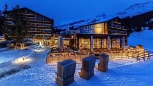 A hotel with a large outdoor seating area, multiple floors, and a mountain backdrop. - Valbella Resort (Vaz-Obervaz)