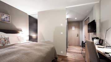 Une chambre d’hôtel comprenant un lit, un bureau avec une chaise, une télévision et une porte donnant sur une autre pièce.