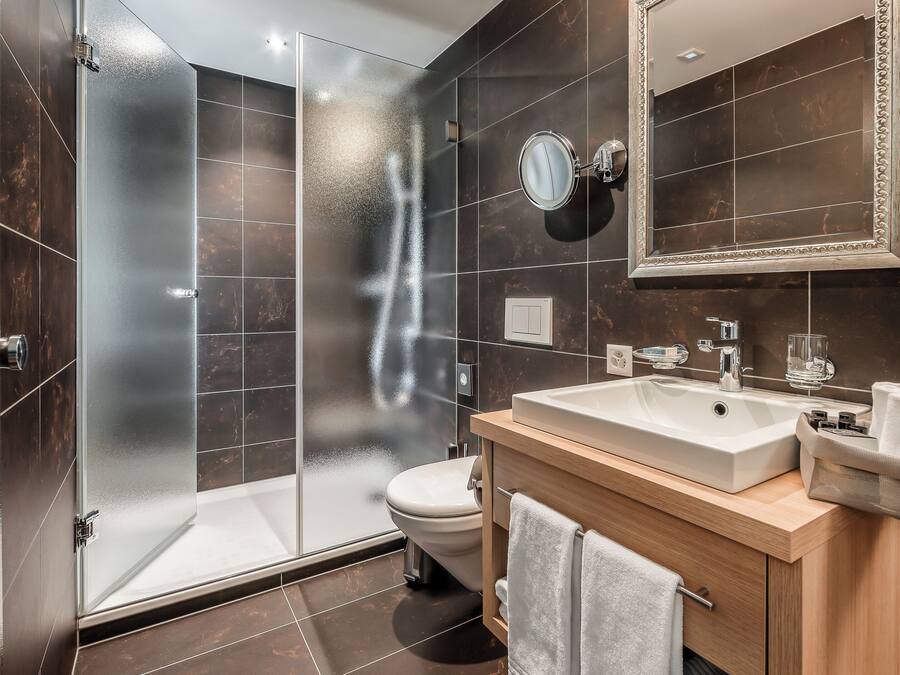 Un baño moderno con ducha envuelta en vidrio, inodoro blanco y tocador de madera con lavamanos.