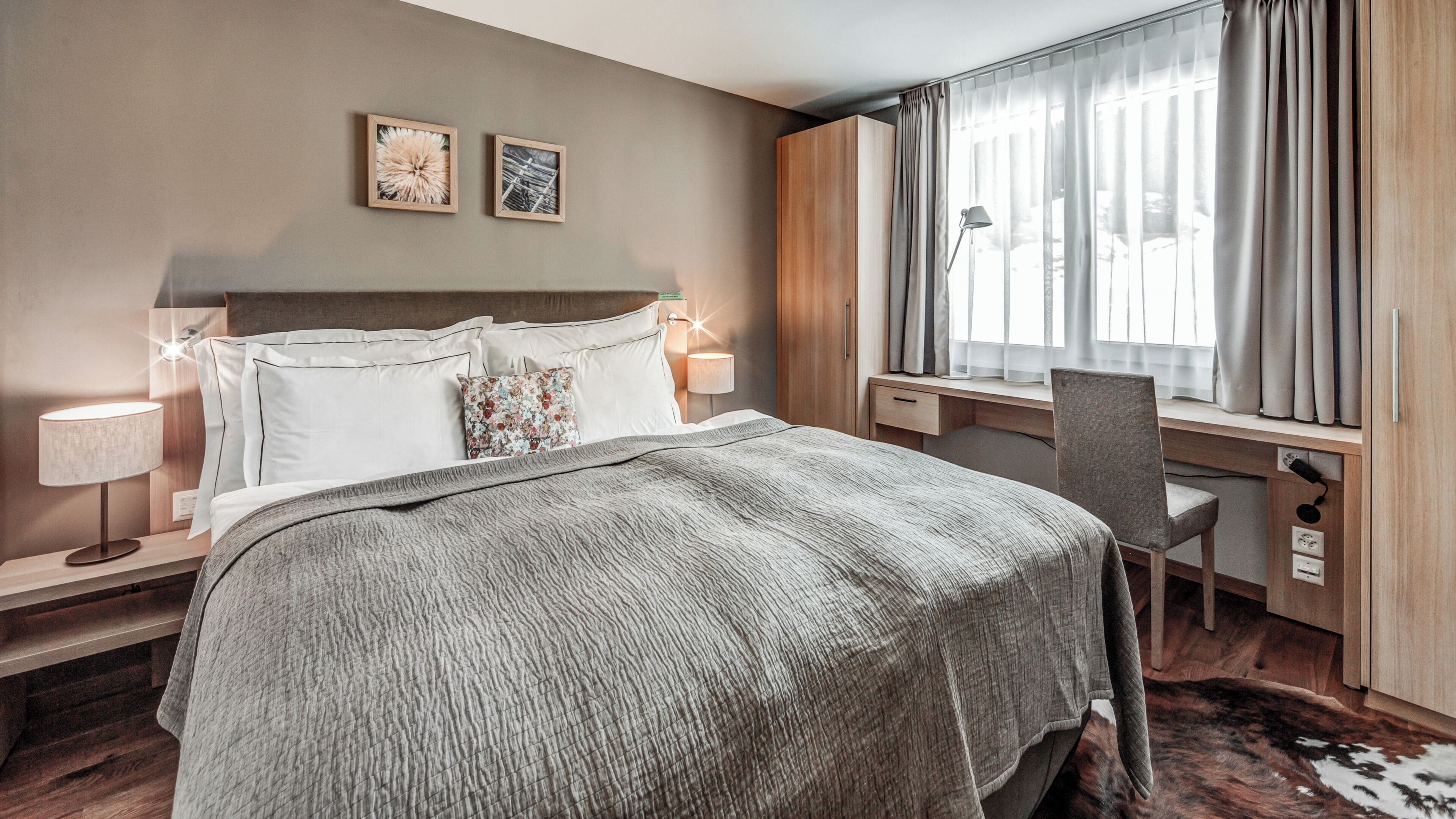 A hotel room with a bed, bedside lamps, a desk, and a window with curtains.