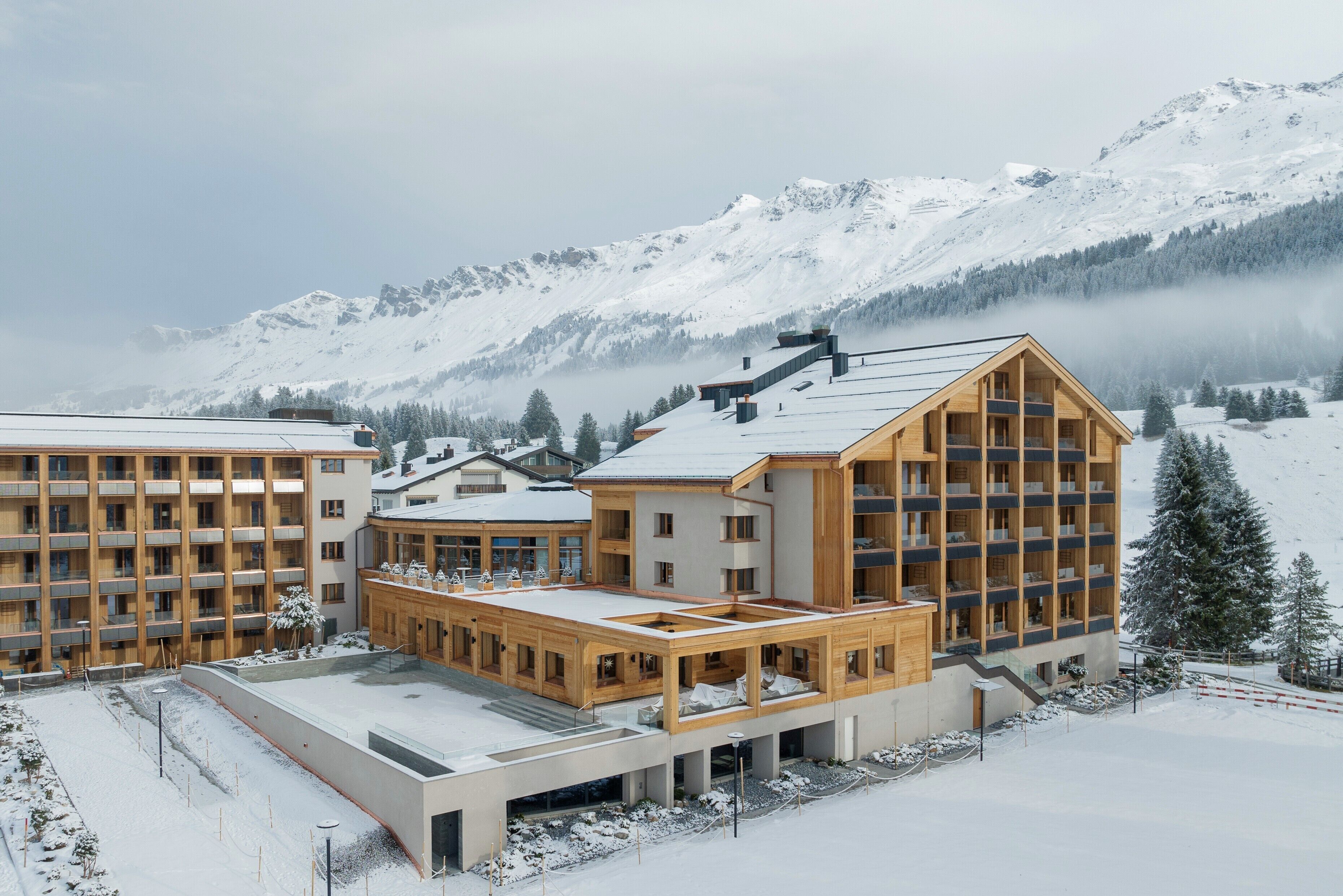 Un hôtel moderne à plusieurs étages, doté de grandes fenêtres et offrant une vue sur un paysage montagneux enneigé.