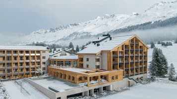 Un hôtel moderne à plusieurs étages, doté de grandes fenêtres et offrant une vue sur un paysage montagneux enneigé.