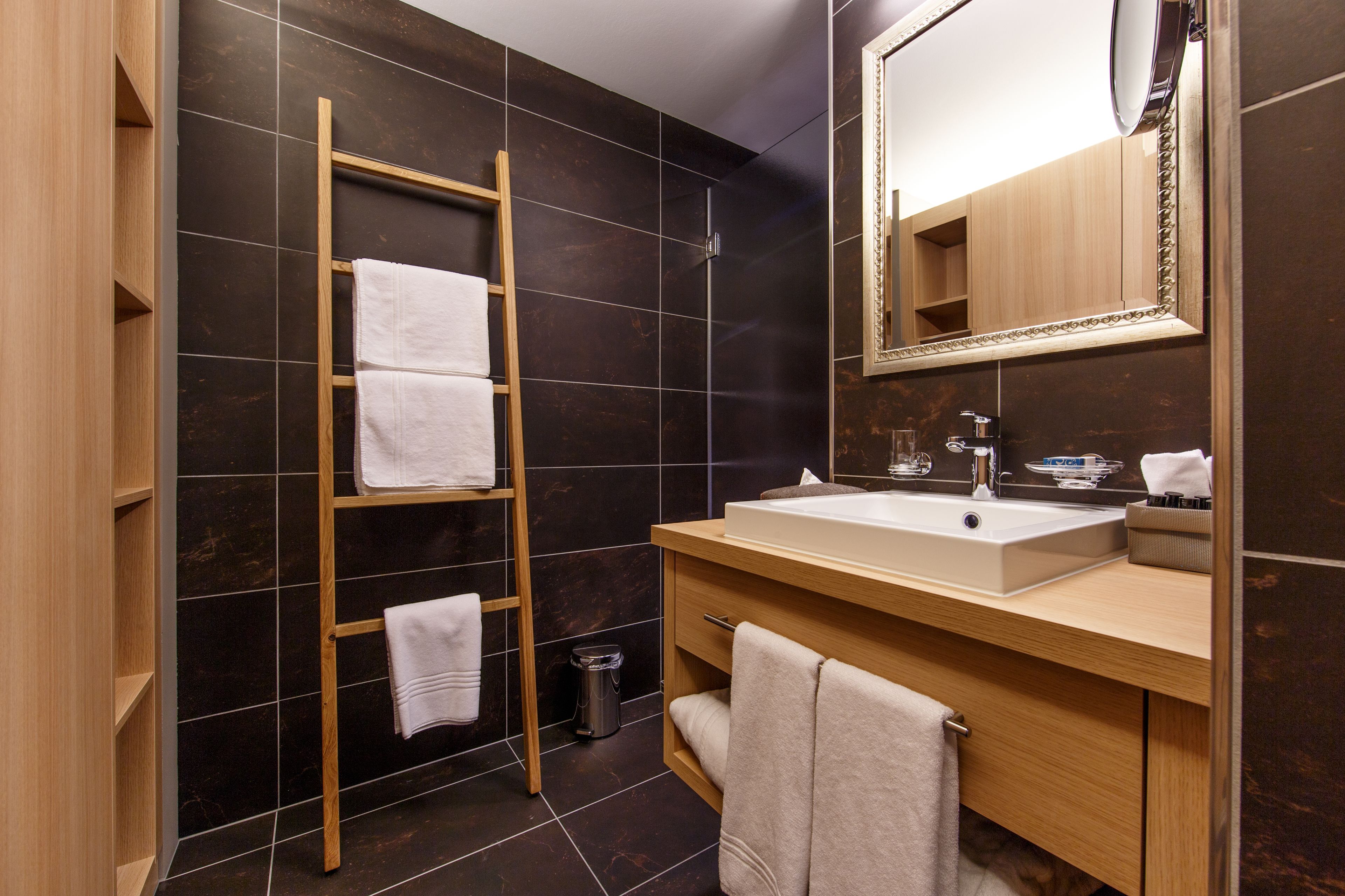 A modern bathroom with a wooden vanity, a large mirror, and a towel rack.