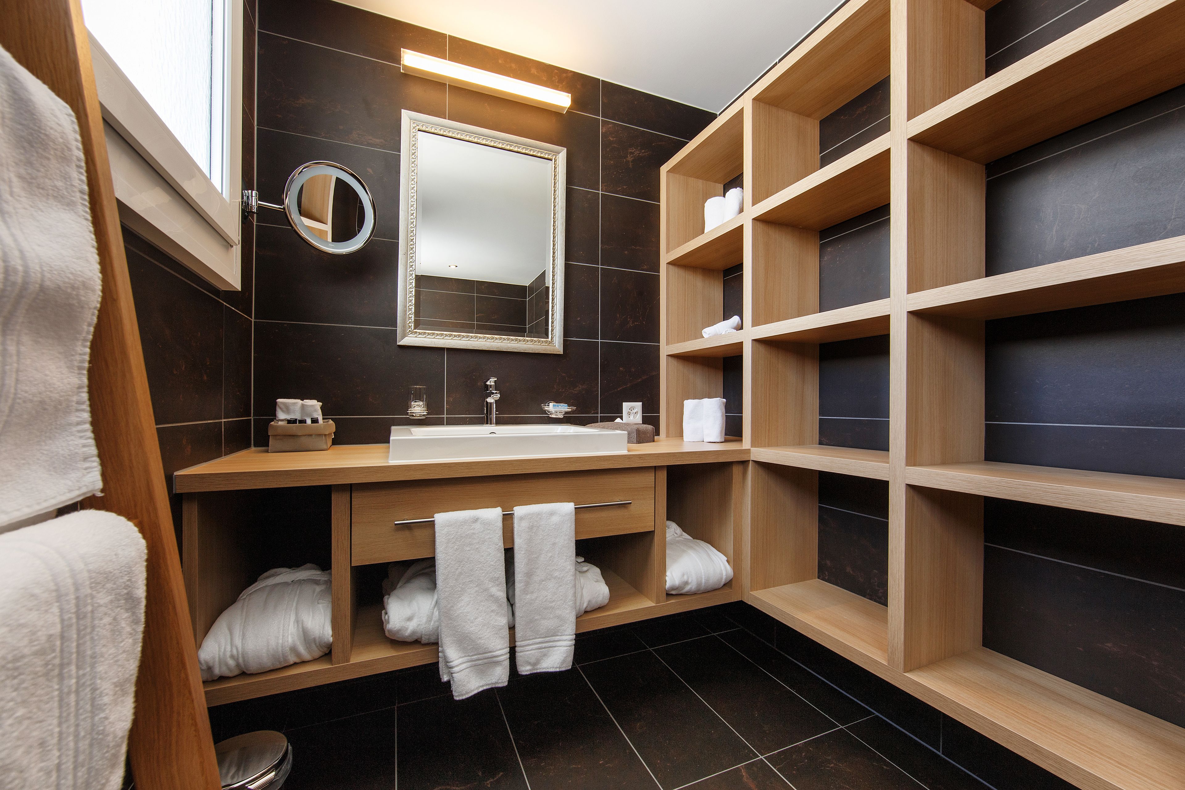 Un bagno moderno con un mobile vanitario in legno, uno specchio grande e scaffali a incasso.