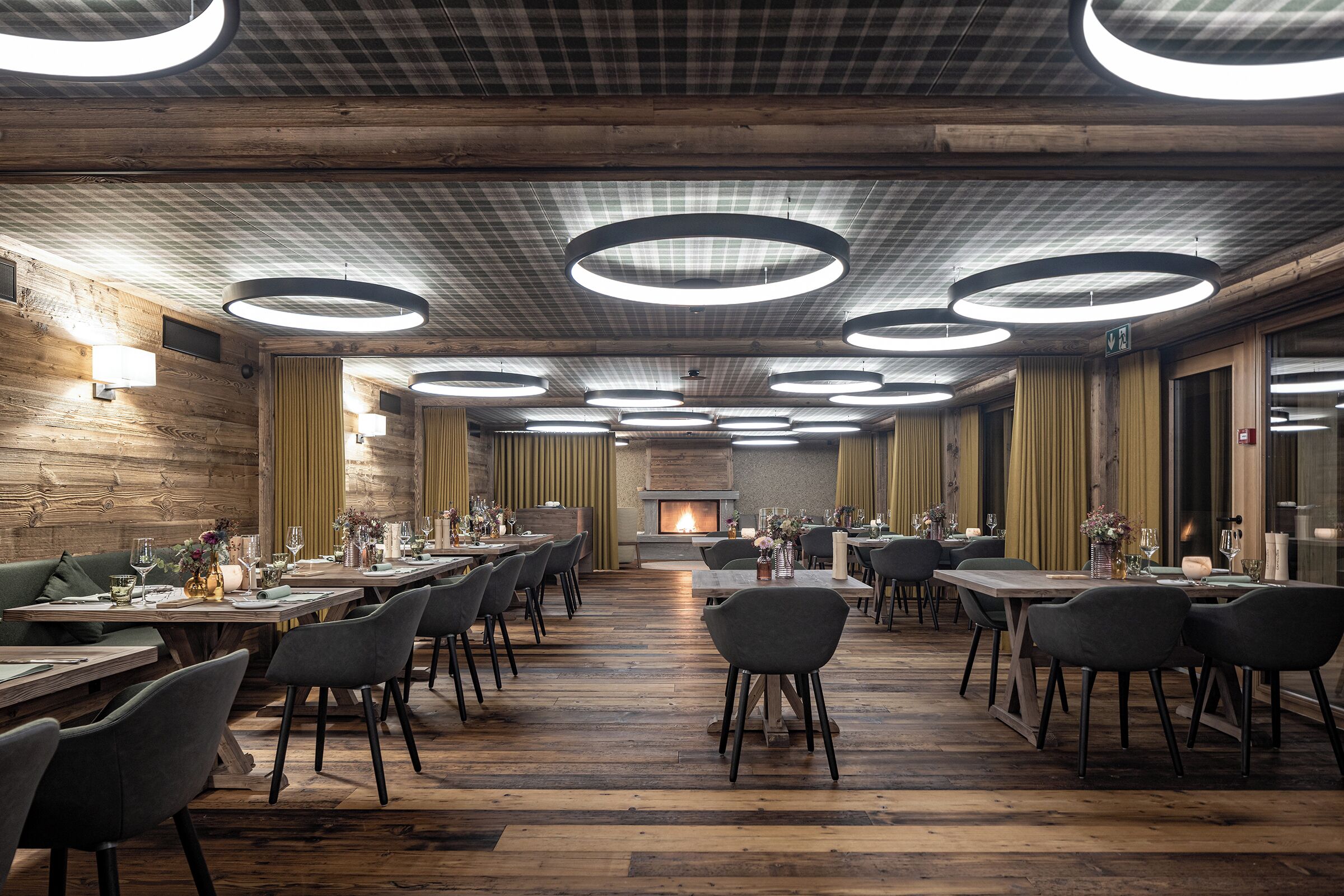 A spacious restaurant with wooden floors, modern circular ceiling lights, and a central fireplace.