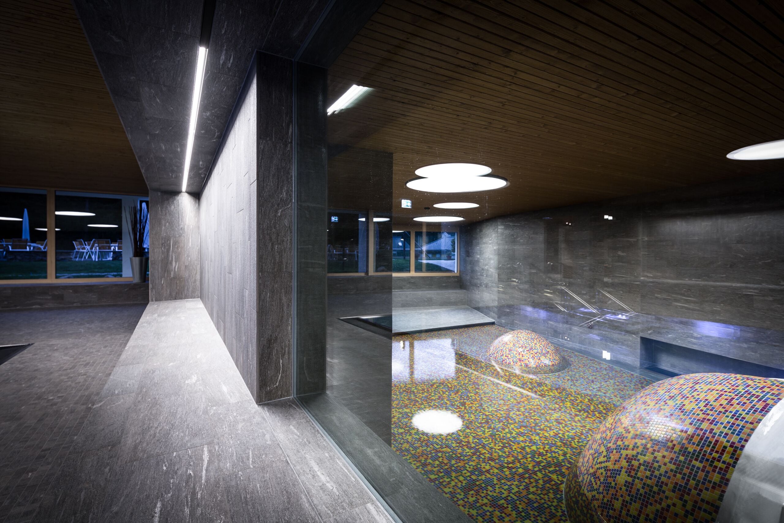 Un interior moderno con piso reflectante, techo de madera y una zona de estar con llamativos diseños de mosaico.