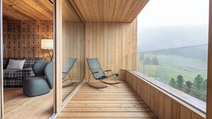 A wooden balcony with a view of a green landscape, a sofa, and two rocking chairs. - Valbella Resort (Vaz-Obervaz)