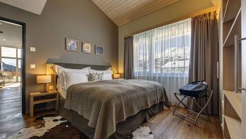 A bedroom with a large bed, a nightstand, a lamp, a window with curtains, and a view of a snowy landscape.