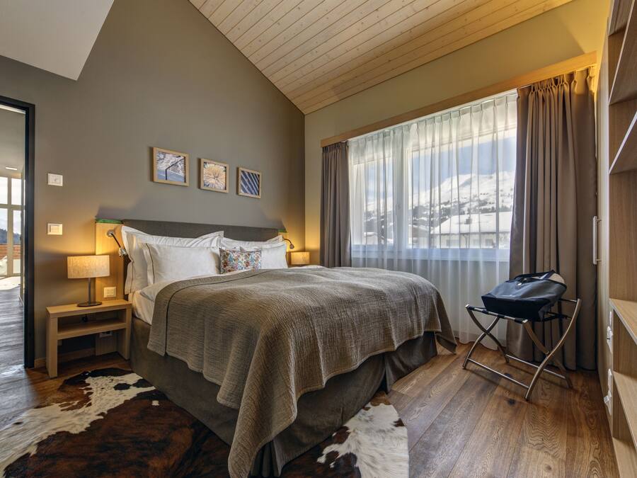 A bedroom with a large bed, a nightstand, a lamp, a window with curtains, and a view of a snowy landscape.
