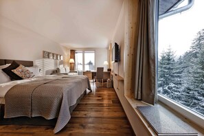 Habitación de hotel con una cama grande, un escritorio y vistas a árboles cubiertos de nieve.