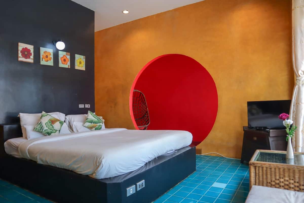 A modern hotel room with a bed, a red circular accent wall, a television, and a small table with a vase.