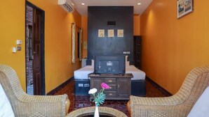Ein Hotelzimmer mit einem Bett, einem Fernseher, einem kleinen Tisch mit Blumenvase, zwei Korbstühlen und einem dunklen Schrank.