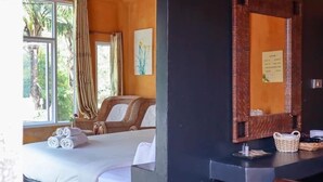 Ein Hotelzimmer mit Bett, Sessel, einem Fenster mit Vorhängen, Spiegel und einem Wandkorb.