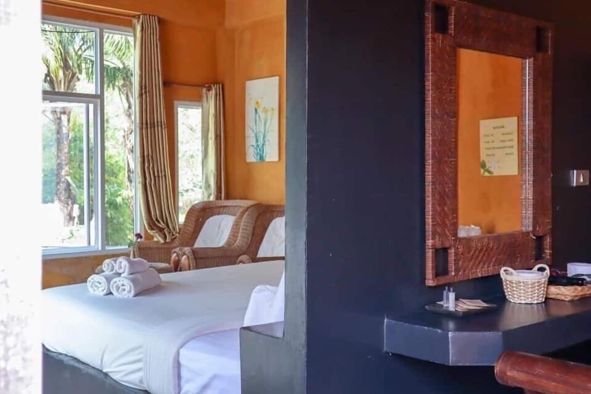 A hotel room with a bed, a chair, a window with curtains, a mirror, and a wall-mounted basket.