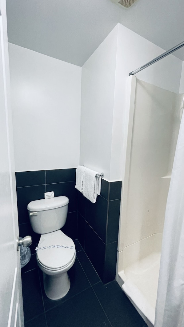 A small bathroom with a toilet, a towel hanging on the wall, and a shower area. - Falcon Motel Brossard (Brossard)