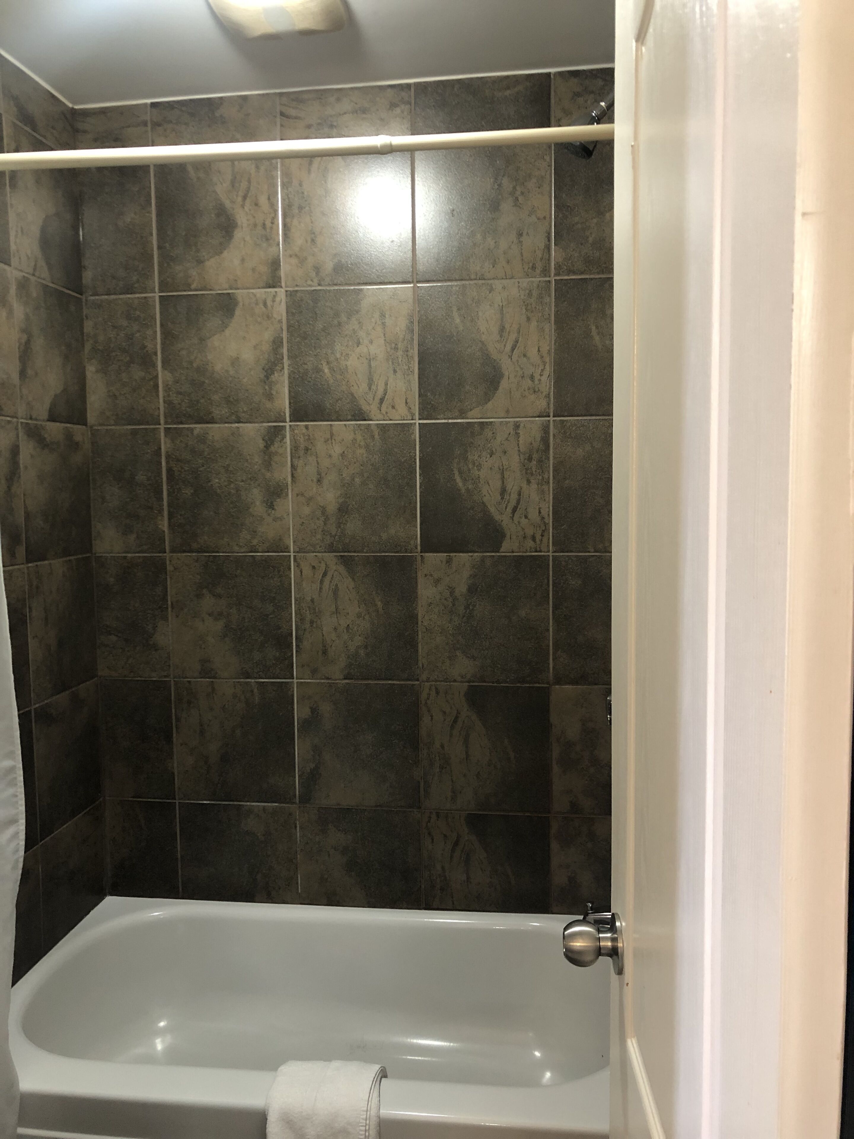 A bathroom with dark stone tiles, a white bathtub, and a visible shower curtain rod.