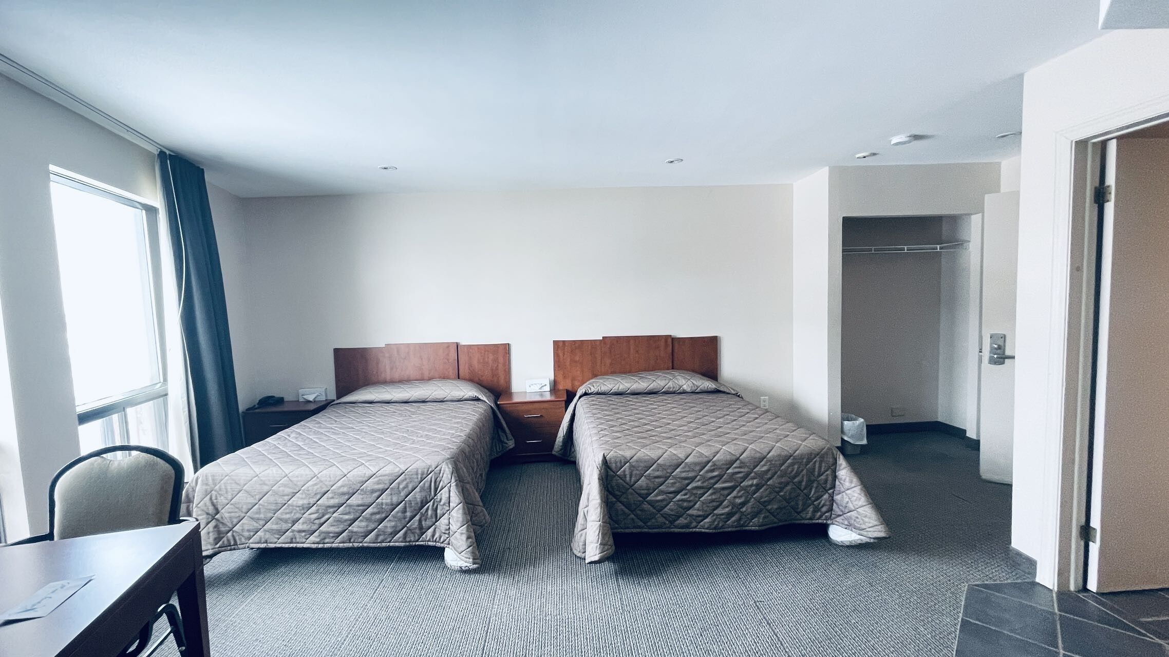 A hotel room with two beds, a desk, and a chair.
