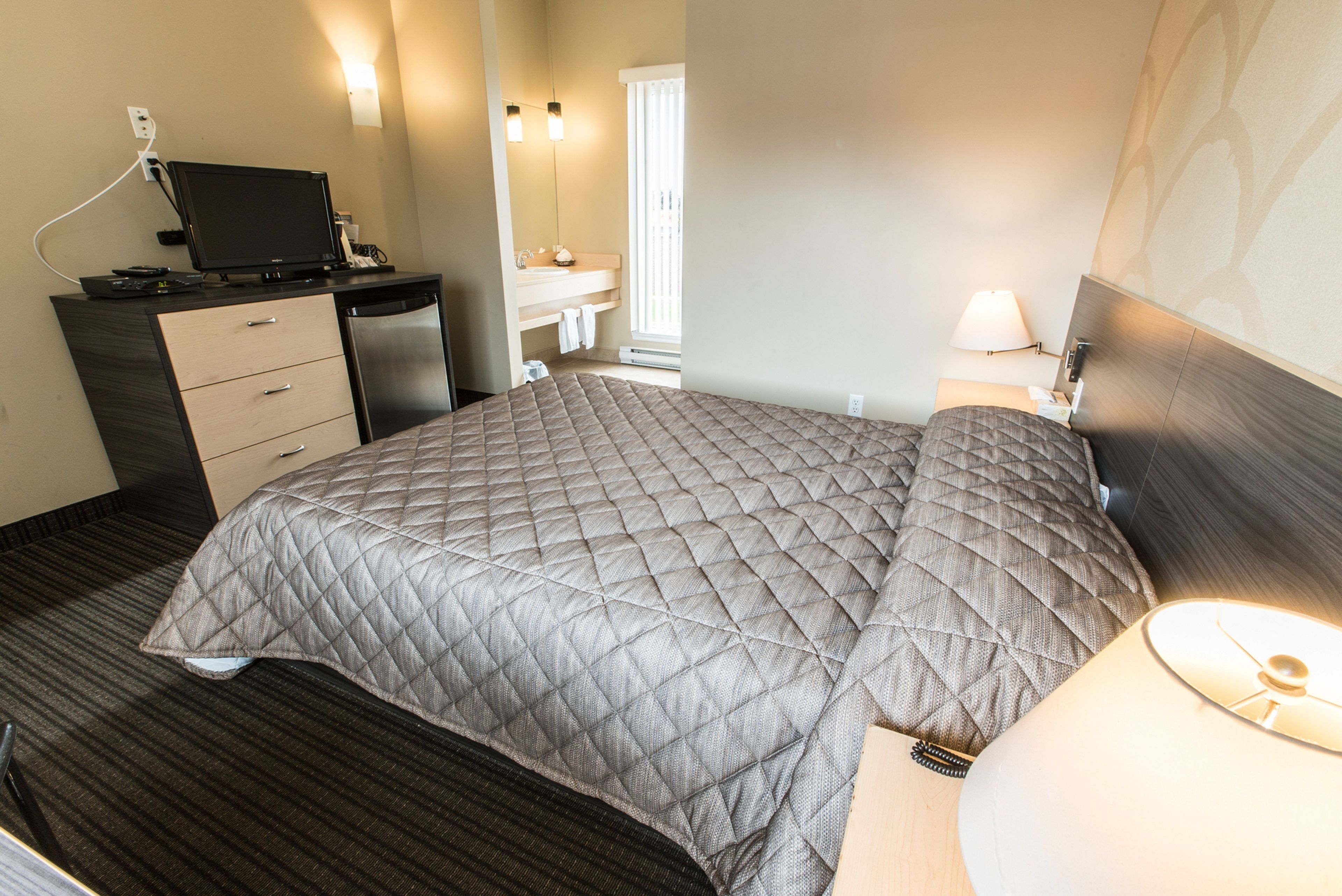 Ein Hotelzimmer mit einem Bett, einem Schreibtisch mit Computer, einem Badezimmer und einem Fenster.