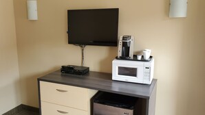 Een kleine kitchenette met een magnetron, koffiezetapparaat en een wandgemonteerde flatscreen televisie.