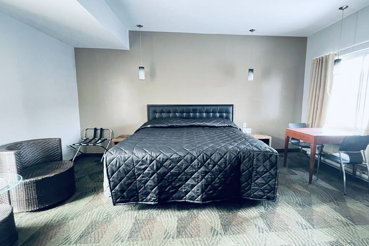 A hotel room with a bed, a desk, a chair, and a window with curtains.