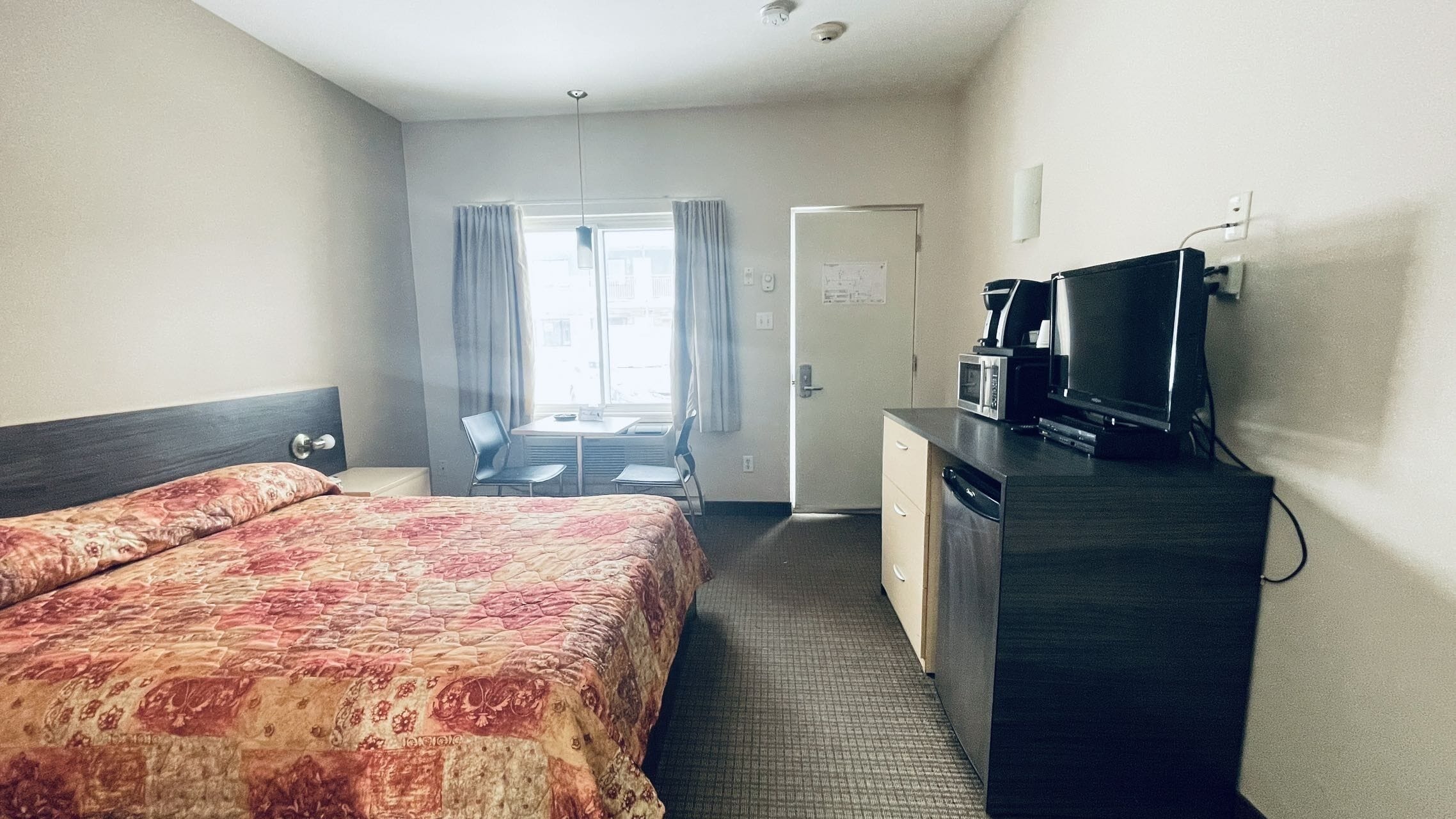 Une chambre d’hôtel comprenant un lit, un bureau avec un micro-ondes, une télévision et une porte donnant sur un balcon.