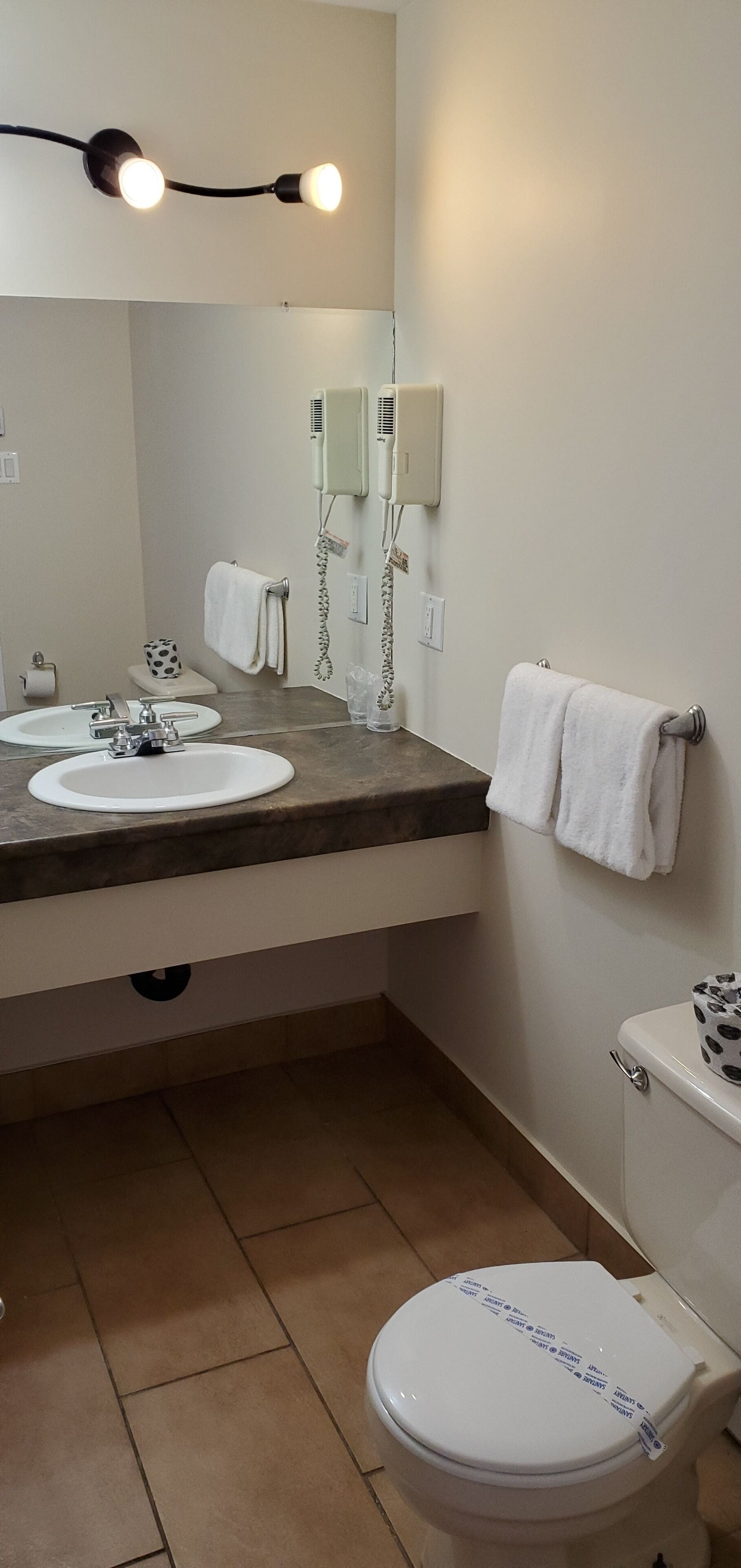 A bathroom with a sink, mirror, towel rack, toilet, and a hairdryer on the wall.