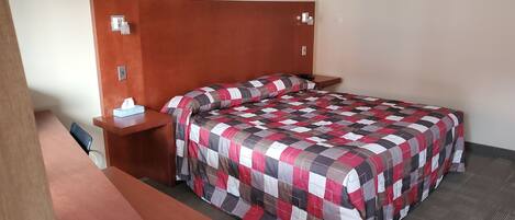 A neatly made bed with a checkered bedspread, a bedside table with a tissue box, and a wooden headboard.