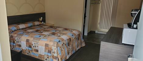 A neatly made bed with a patterned bedspread, a bedside table with a lamp, and a window with blinds.