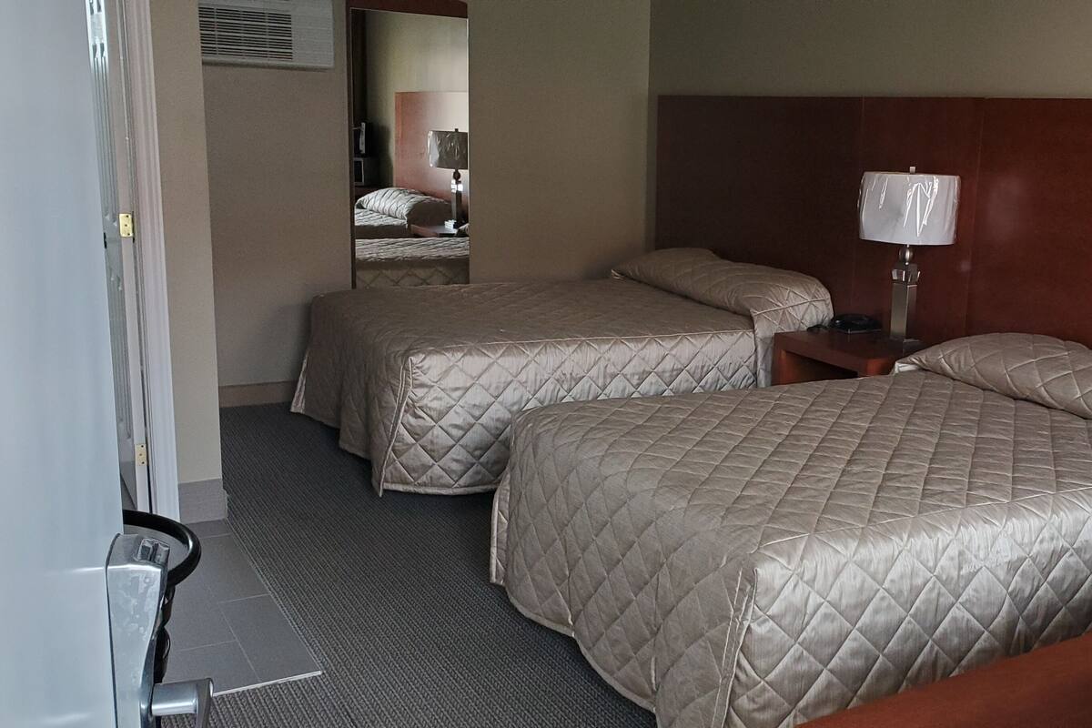 A hotel room with two beds, a nightstand with a lamp, and a mirror on the wall.