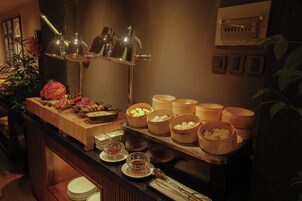 A buffet setup with various food items and bowls, a lamp, and a wall-mounted electrical panel.