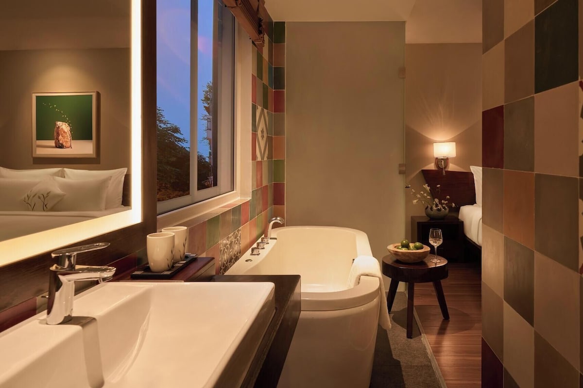 A modern bathroom with a bathtub, a large mirror, and a window.