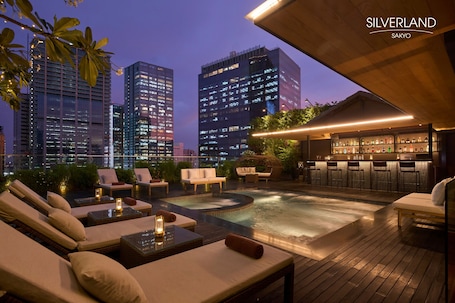 A rooftop bar with a pool, lounge chairs, and a bar area with stools.