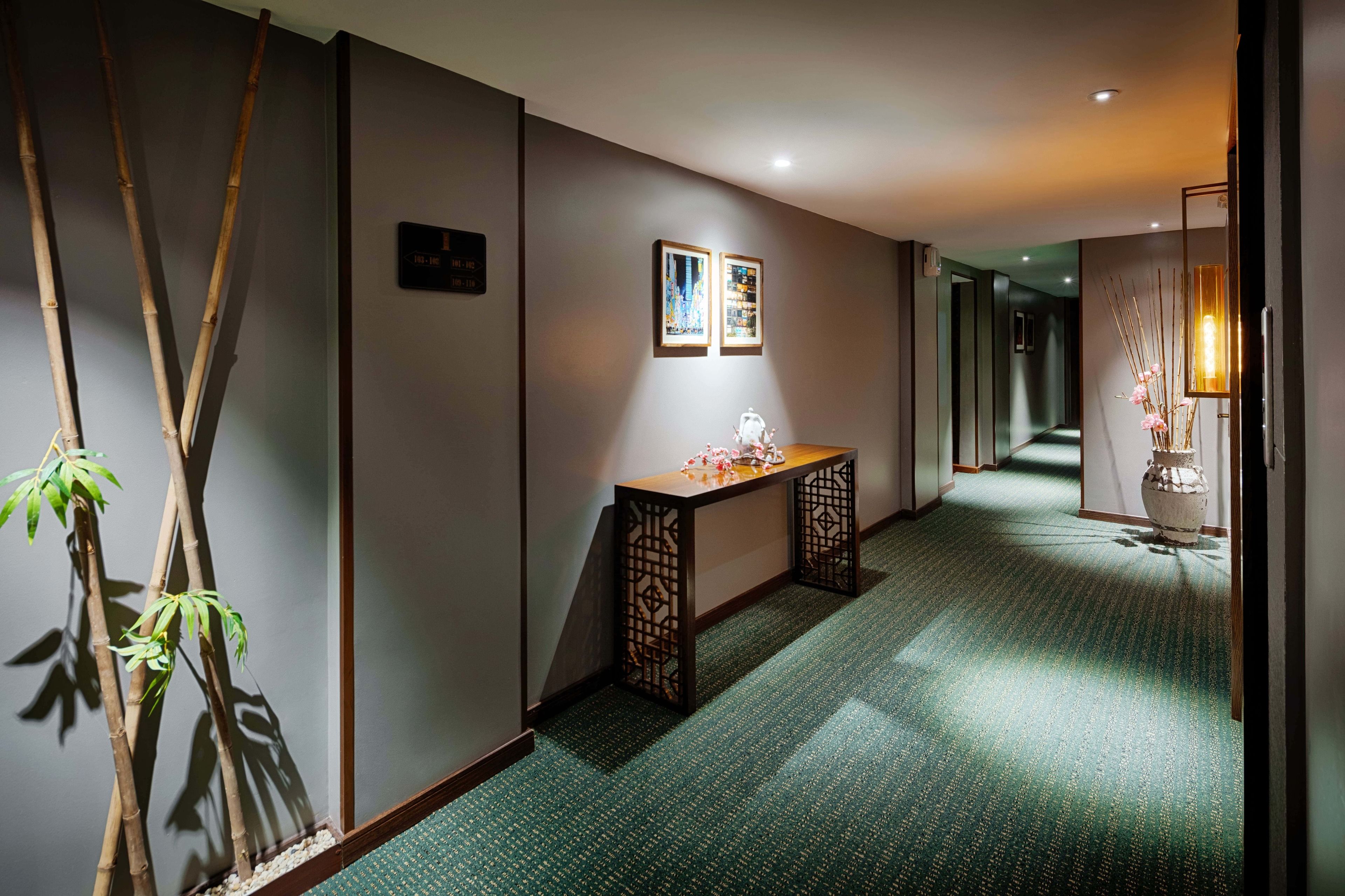 A hallway with a green carpet, a wooden bench, and a vase with flowers.