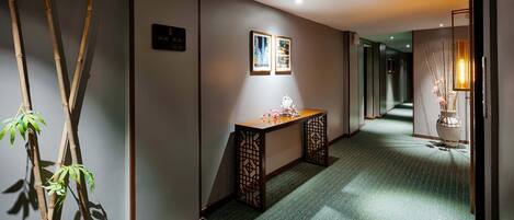 A hallway with a green carpet, a wooden bench, and a vase with flowers.