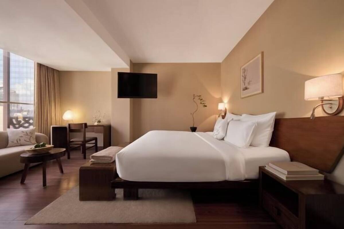 A hotel room with a large bed, a sofa, a desk, a TV, and a window.