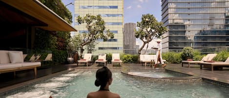 Área de piscina en la azotea con sillones reclinables, un camarero y vistas panorámicas de la ciudad.