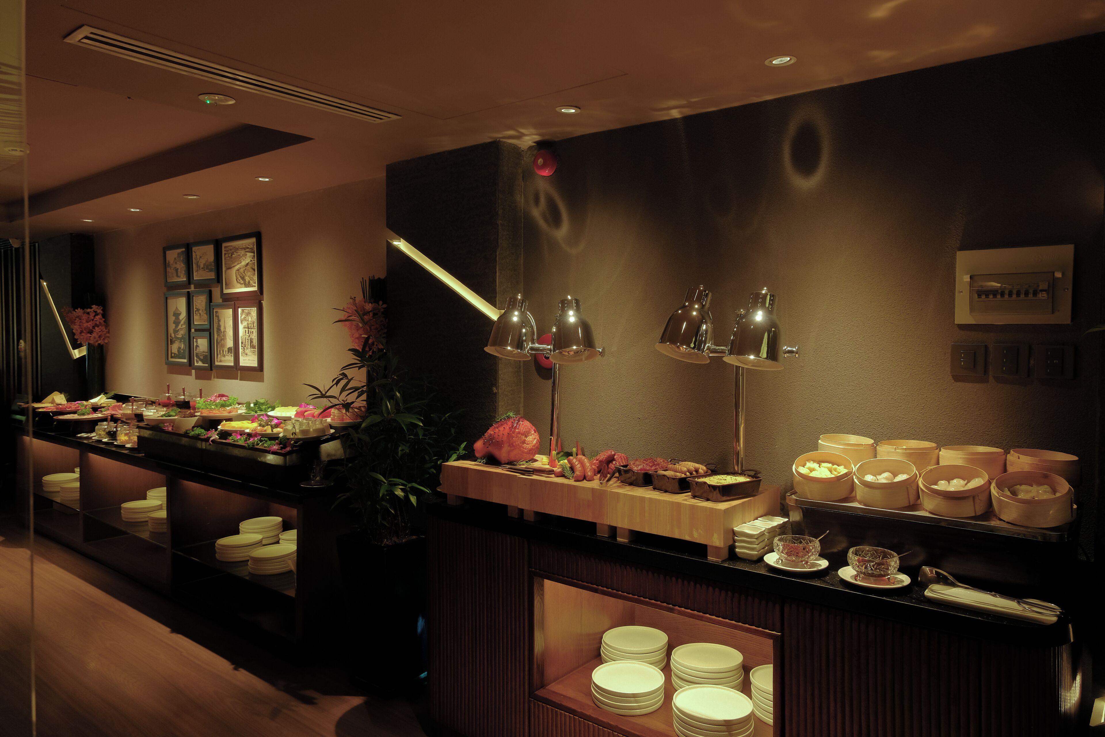 A buffet setup with various food items and dishes, a wall-mounted picture frame, and a potted plant.
