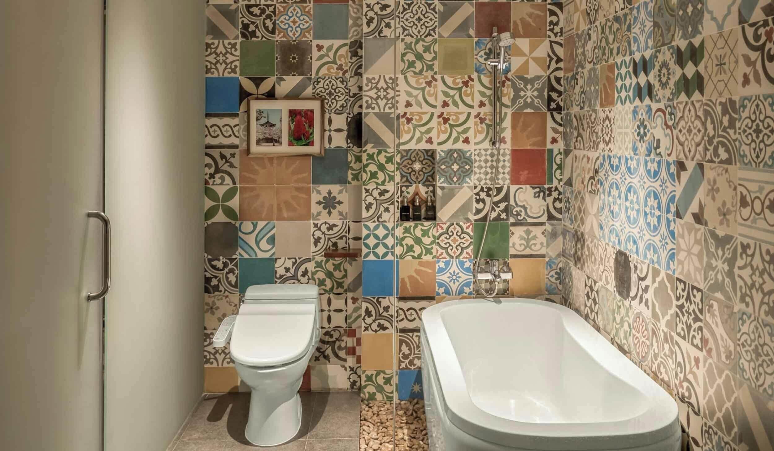 Une salle de bain comprenant des toilettes, une baignoire et une douche. Les murs sont recouverts de carreaux aux motifs et aux couleurs variés.