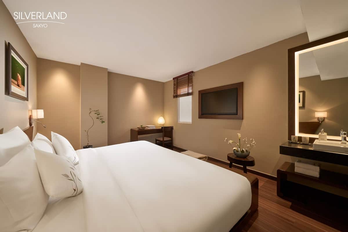 A hotel room with a large bed, bedside table, lamp, and a mirror.