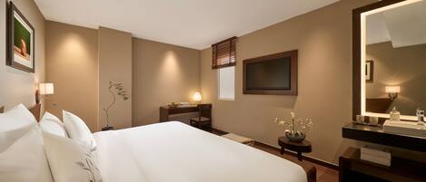 Una habitación de hotel con una cama grande, mesita de noche, lámpara y un espejo.