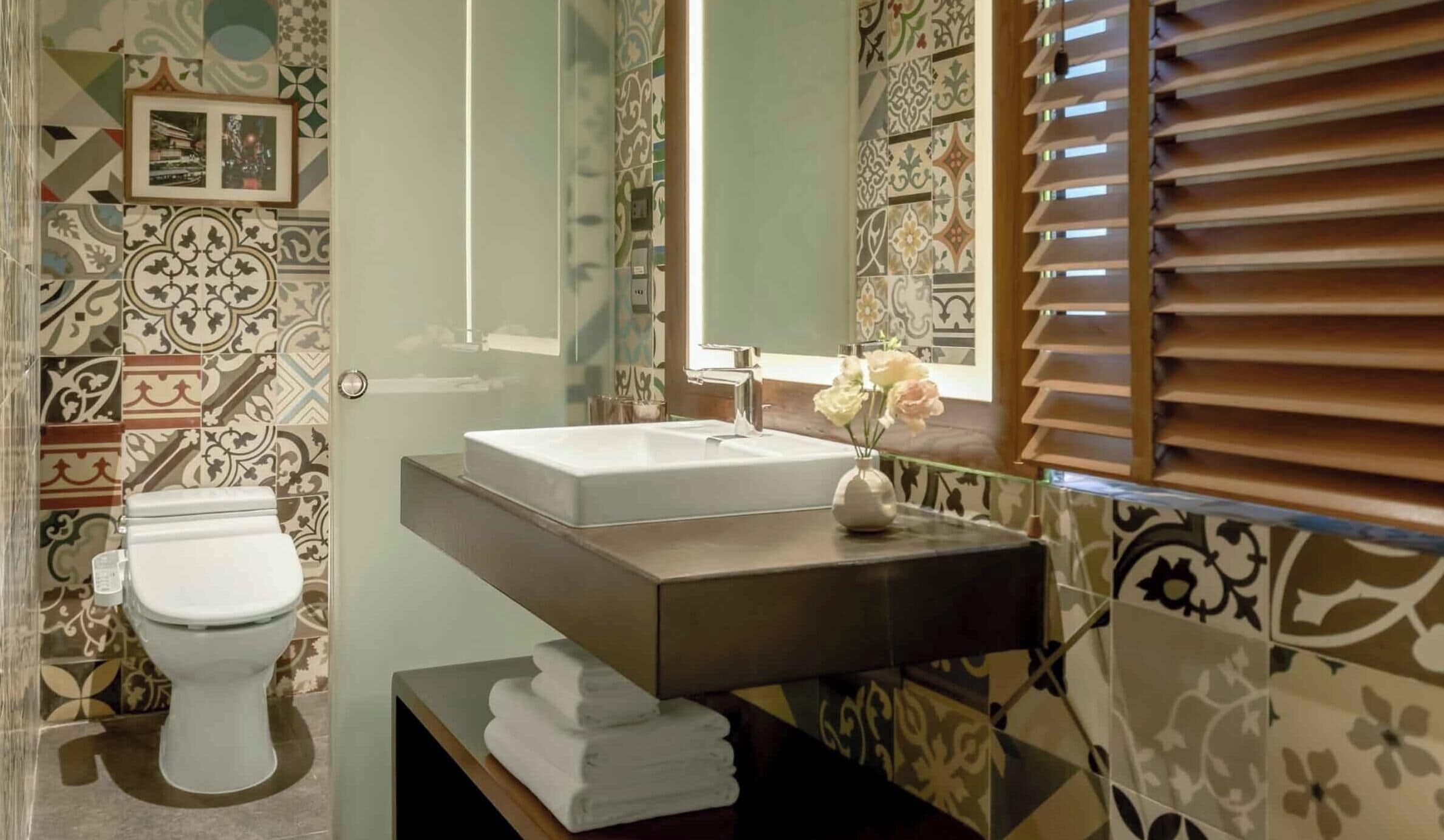 A bathroom with a toilet, sink, mirror, and patterned tiles.