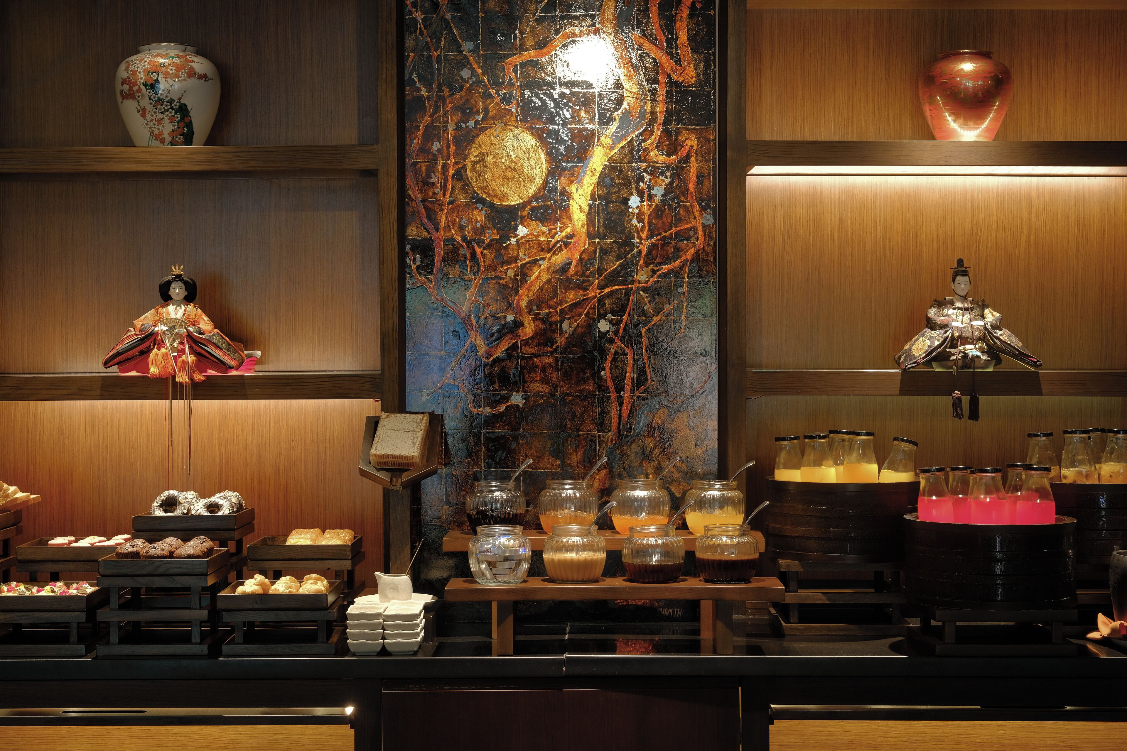 A buffet area with various food items and beverages, a decorative vase, and a traditional doll.