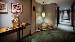 Un pasillo de hotel con un mostrador de recepción de madera, un florero con flores rosas, una lámpara colgante y piso alfombrado.